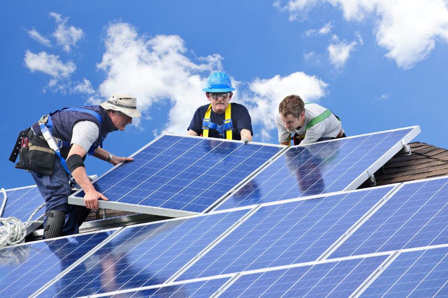 Workers installing solar panels on house roof
